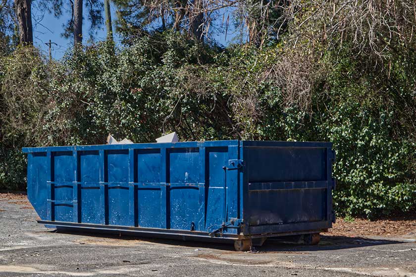 A blue open top dumpster filled with waste on a vacant